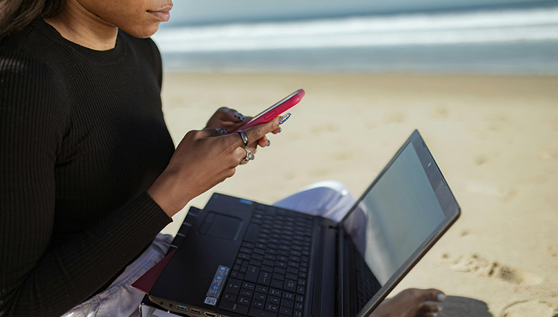 woman at beach using laptop and phone